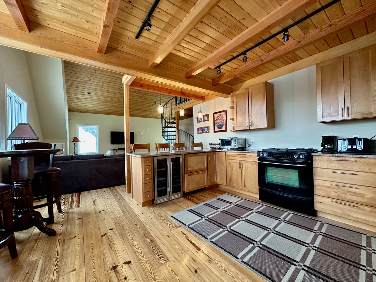 An open concept kitchen and dining area with a kitchen island, stove, spiral staircase, rustic wooden beams, and a large, welcoming dining space. The area is clearly set for socializing, with a cozy and inviting atmosphere ideal for group dinners and holiday celebrations.