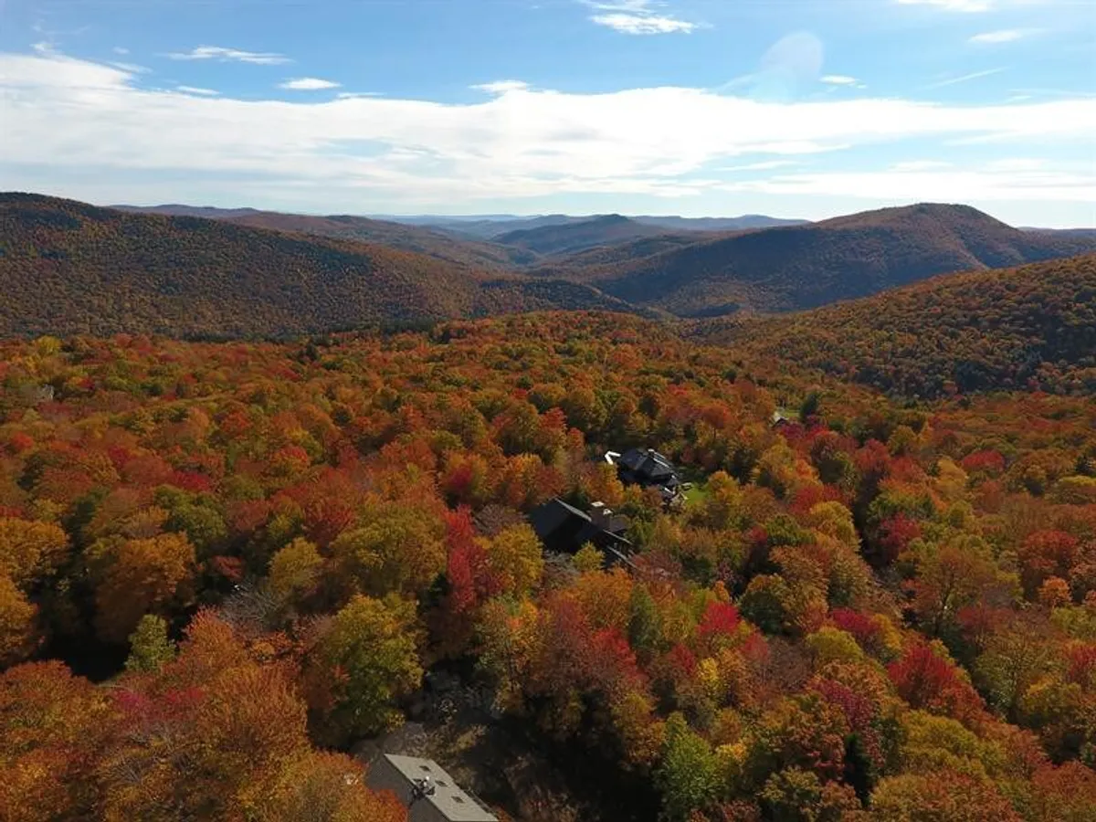 A panoramic view of vibrant autumn foliage, distant mountains, and scattered homes. The tranquil scene highlights the property’s setting amid natural beauty, perfect for hiking and enjoying seasonal changes.