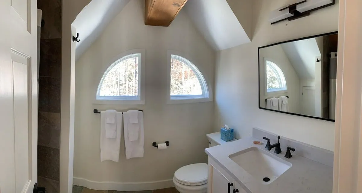 A serene bathroom featuring arched windows that flood the space with natural light, a wooden beam, and a vanity with a sink. The atmosphere is peaceful, perfect for morning routines or a moment of self-care.